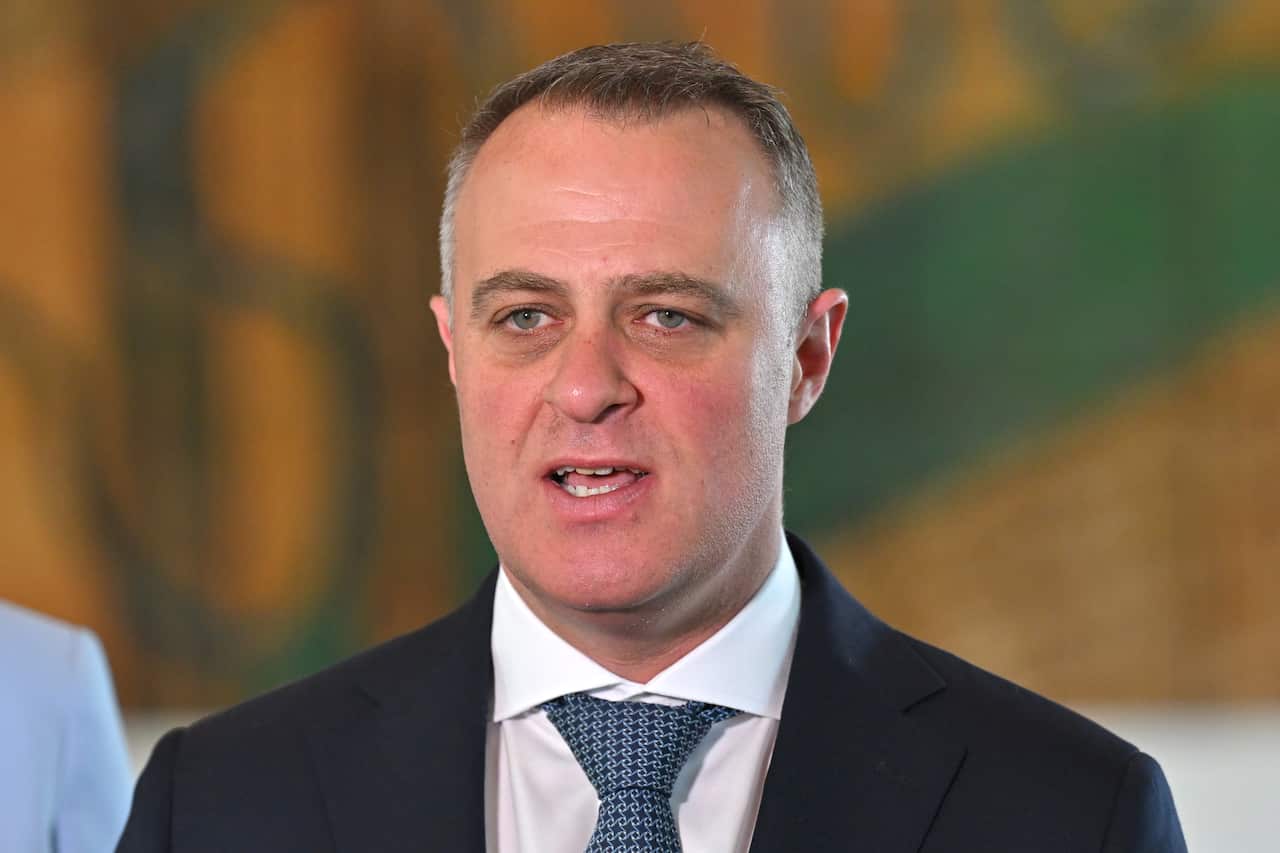 A man wearing a black suit, white shirt and blue tie.