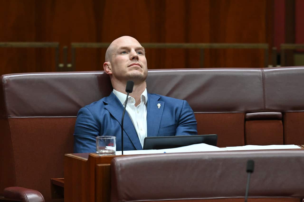 Senator David Pocock, in a blue suit and white shirt, leans back into his seat, staring off into the distance.