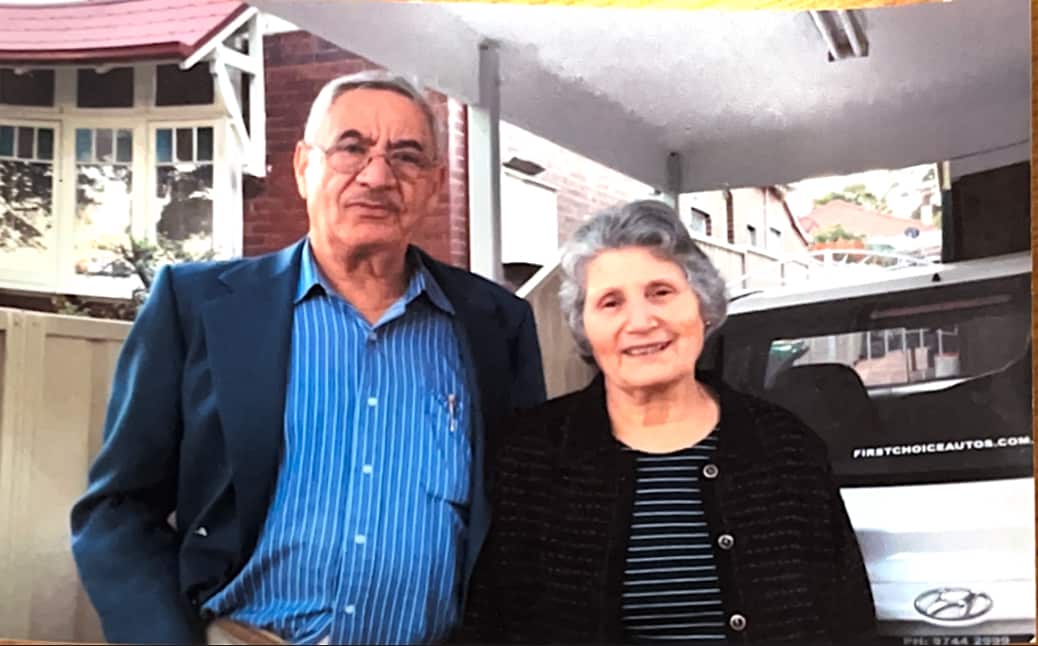 An elderly couple posing for a photo outside their house.