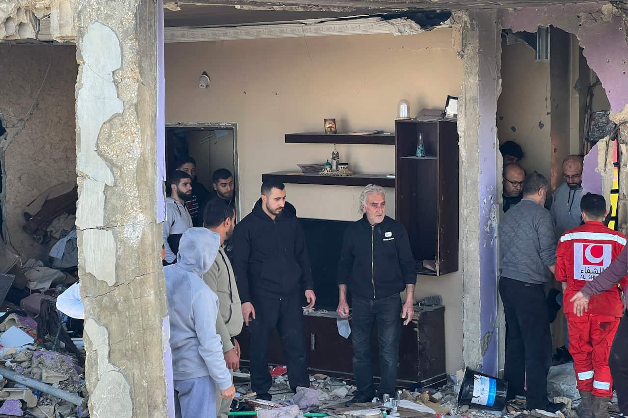 A group of people and emergency workers stand inside a damaged building with exposed walls and debris.
