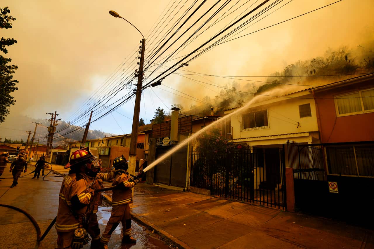 Firefighters spray water onto the roof a house to protect it from fires burning nearby.