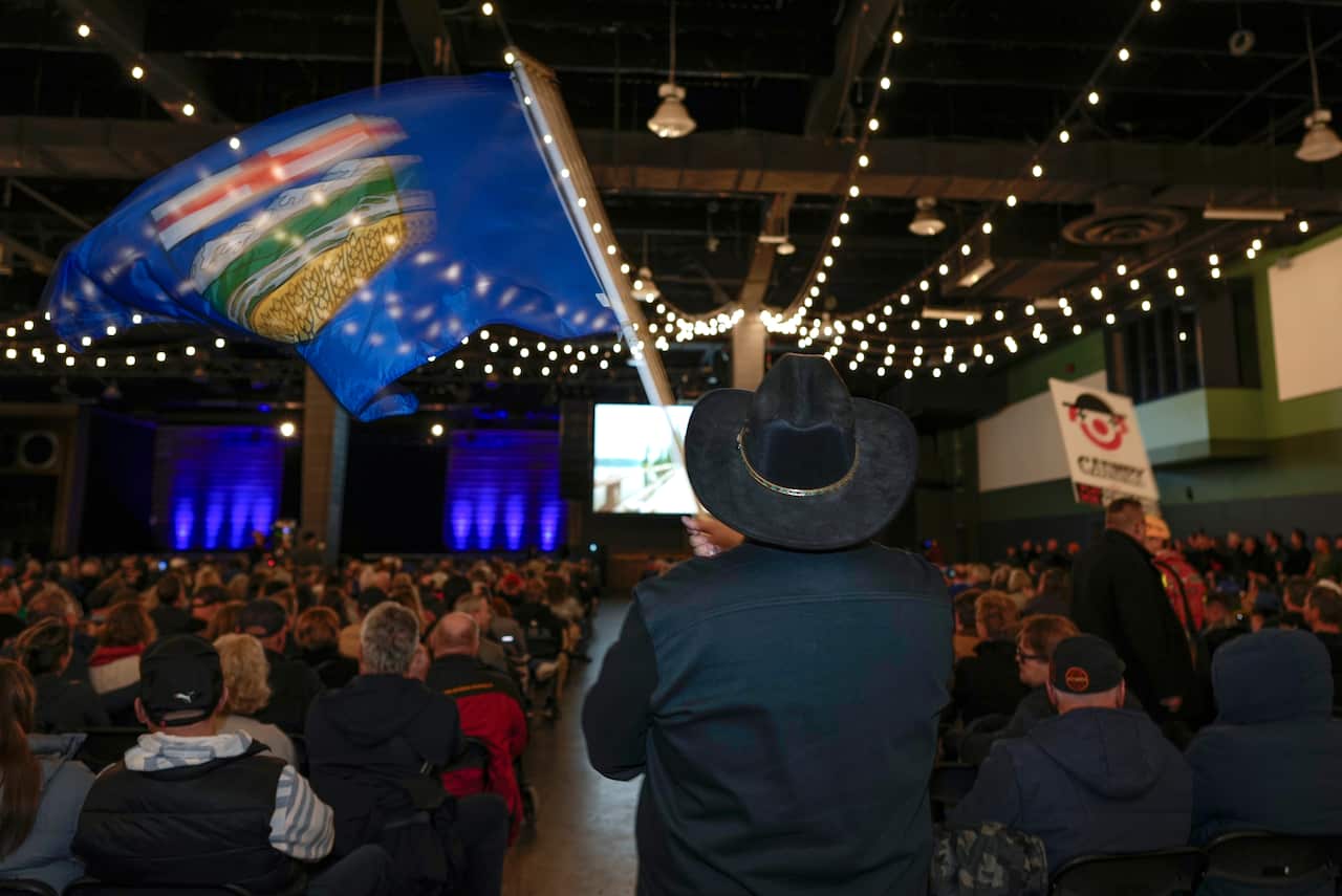 A man waving an Alberta flag wears a cowboy hat at an Alberta separatist event.