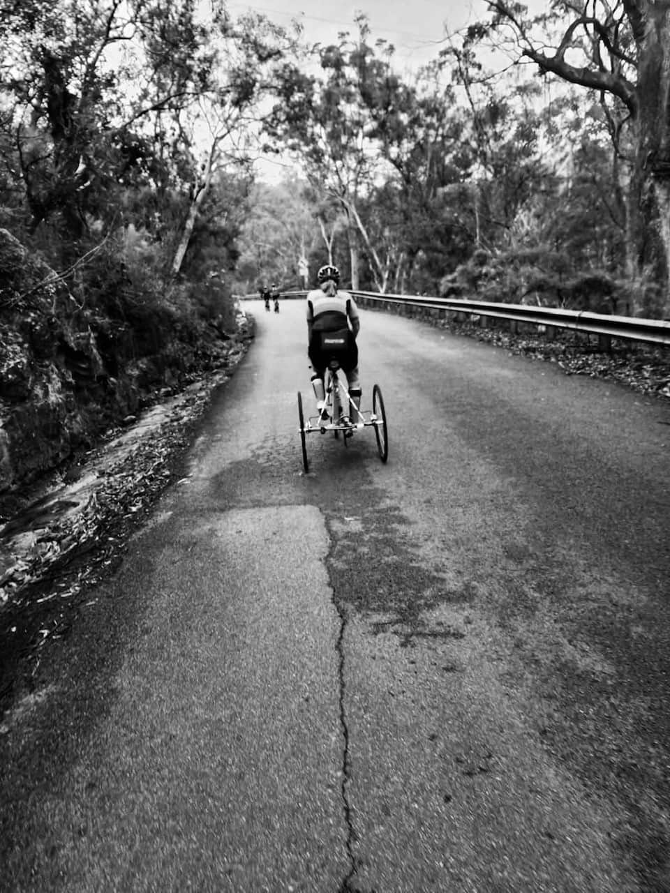 Gabby Vassallo is seen from behind while cycling up a hill in a black and white photo.