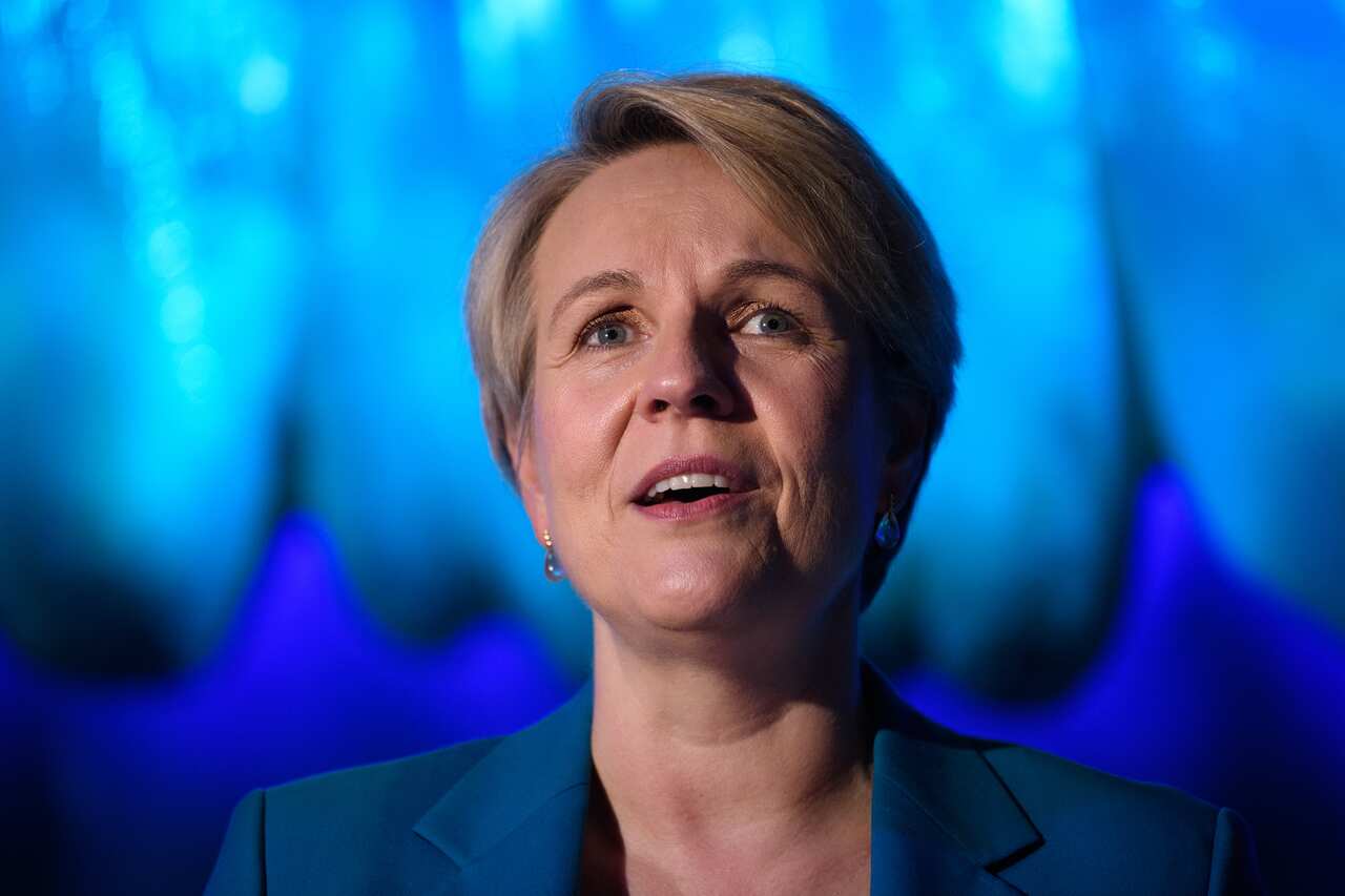Woman in blue jacket speaks in front of aquarium tank.