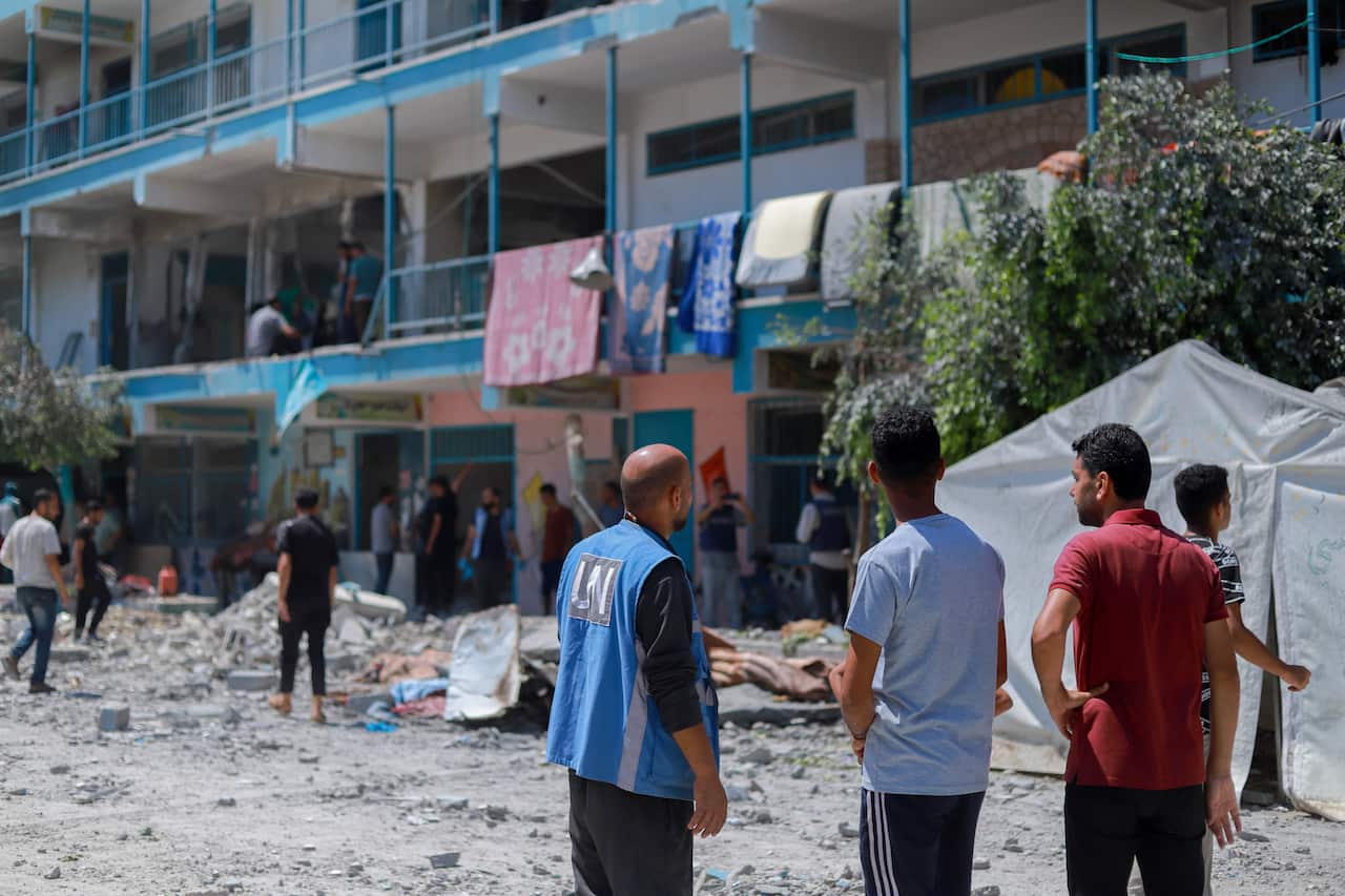 People stand near a building that has been attacked. One is a UN vest.