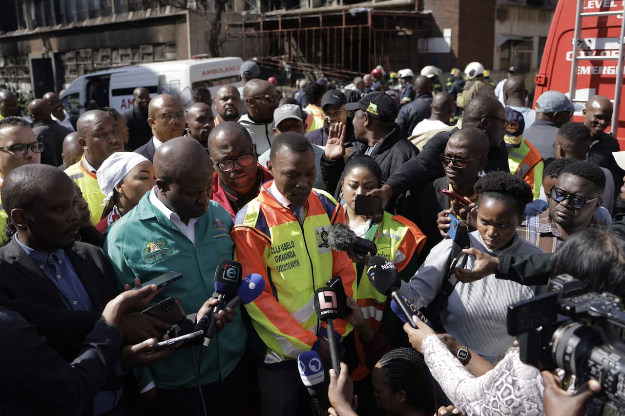 A man speaks to the media as several people look on.