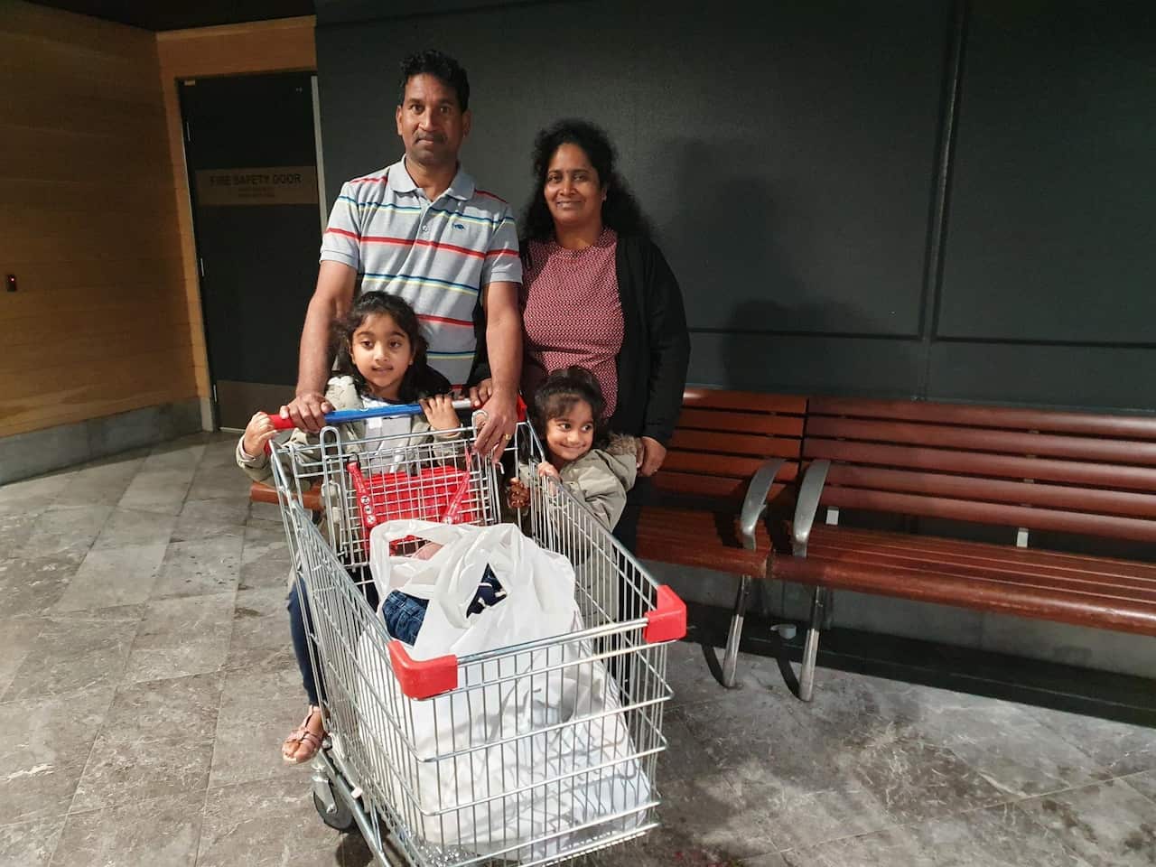 A man and a woman standing with two girls standing in front of them. There is a shopping trolley in front of them.