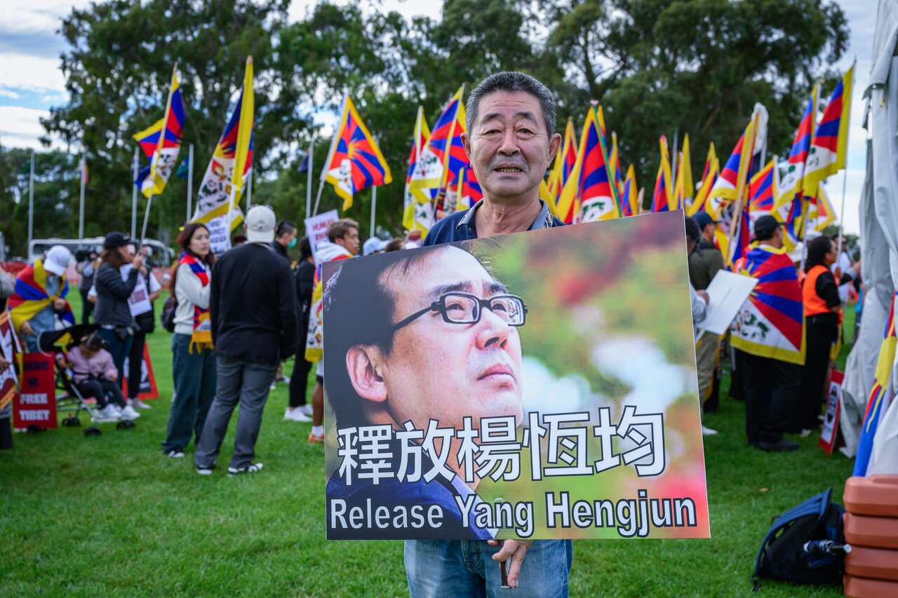 A protester holds a "Release Yang Hengjun" placard during a demonstration, and people are holding flags in the background.