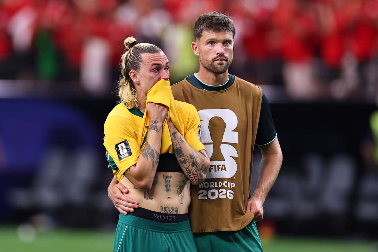 A football player in a green and yellow jersey is comforted by a teammate
