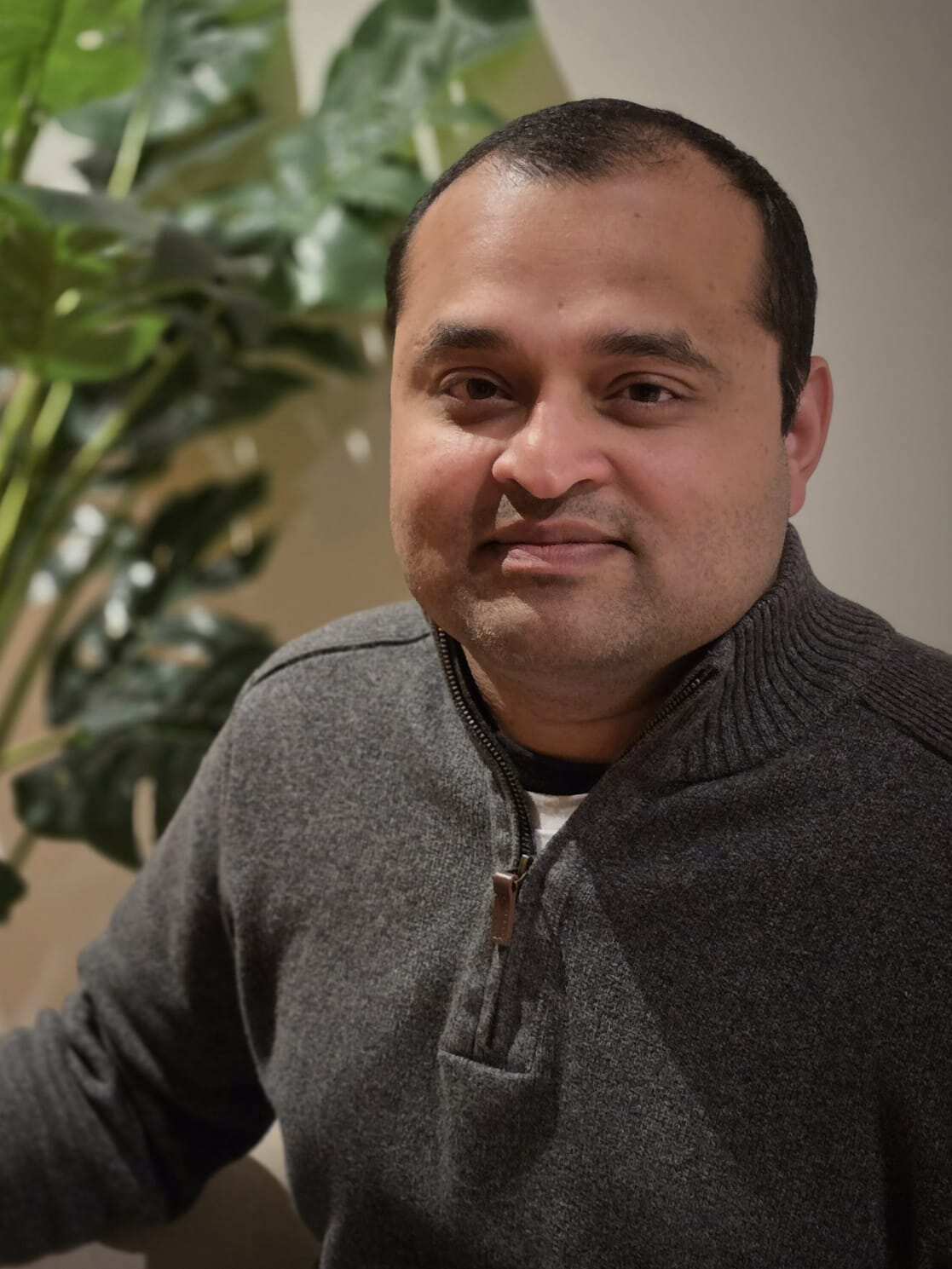 A man in a grey jumper sits facing camera.