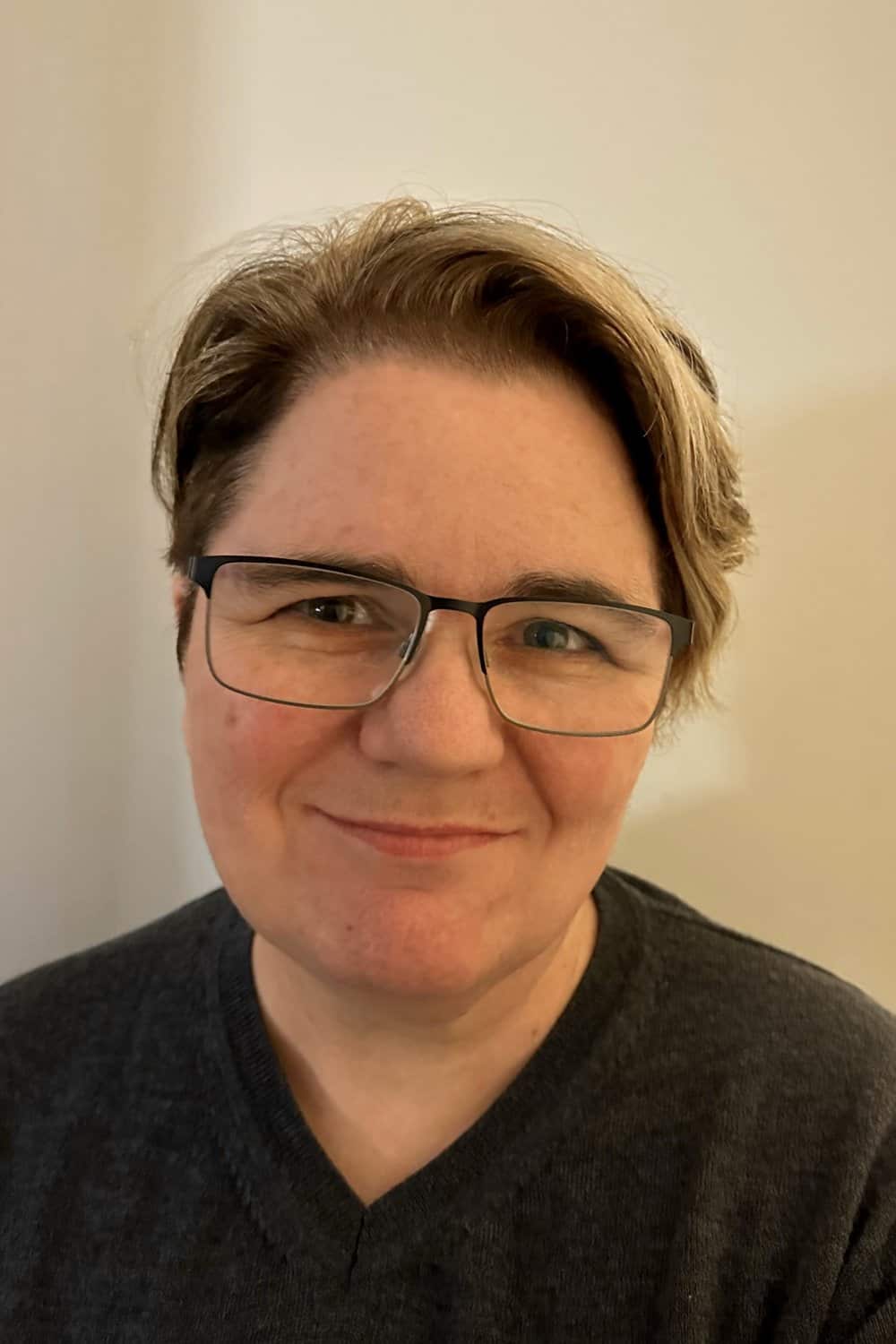 A person wearing a black v-neck shirt and glasses smiles