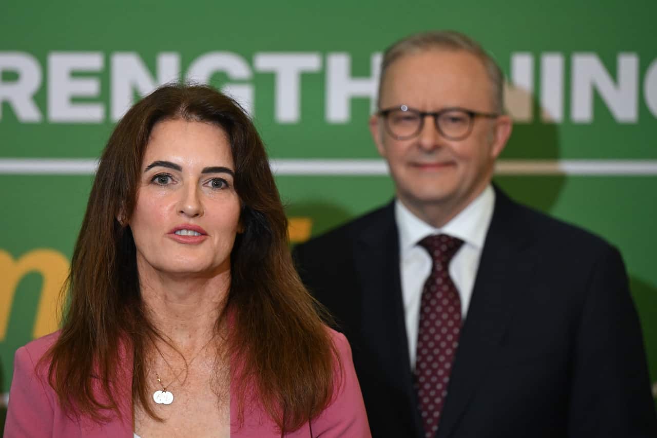 A woman in a pink jacket in focus, with a man in a suit in the background.