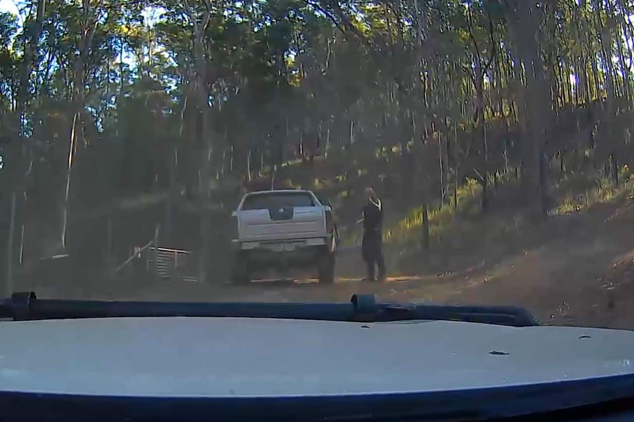A man standing next to a large white ute holds a gun