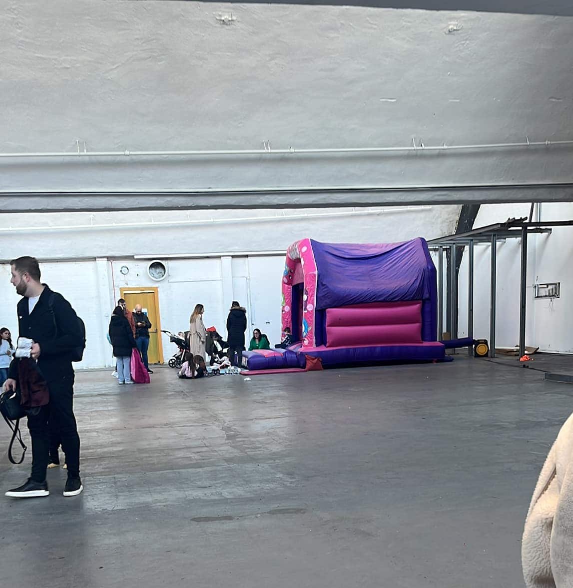 Parents and children in front of a jumping castle that is inside a large warehouse.