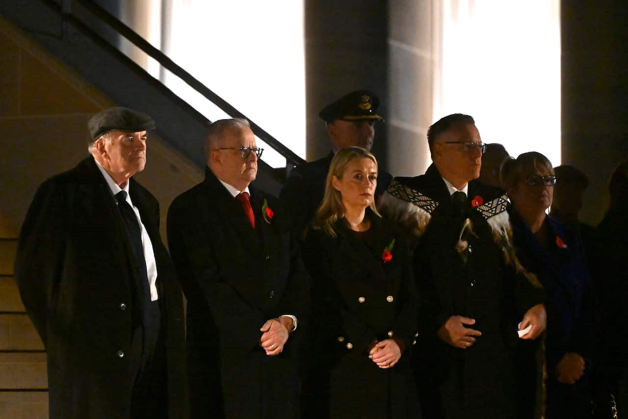 Several men and a woman stand in a line looking solemn.