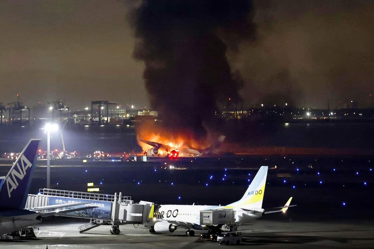 An airport with a plane in the distance on fire.