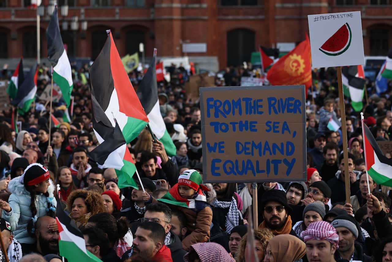 A large group of protesters wave Palestinian flags. One person has a sign that says: "From the river to the sea, we demand equality".