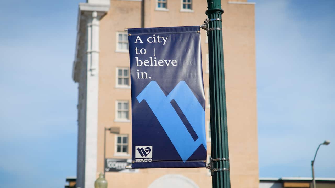 A sign hanging from a lamppost which reads 'A city to believe in.' At the bottom is a Waco County logo. 