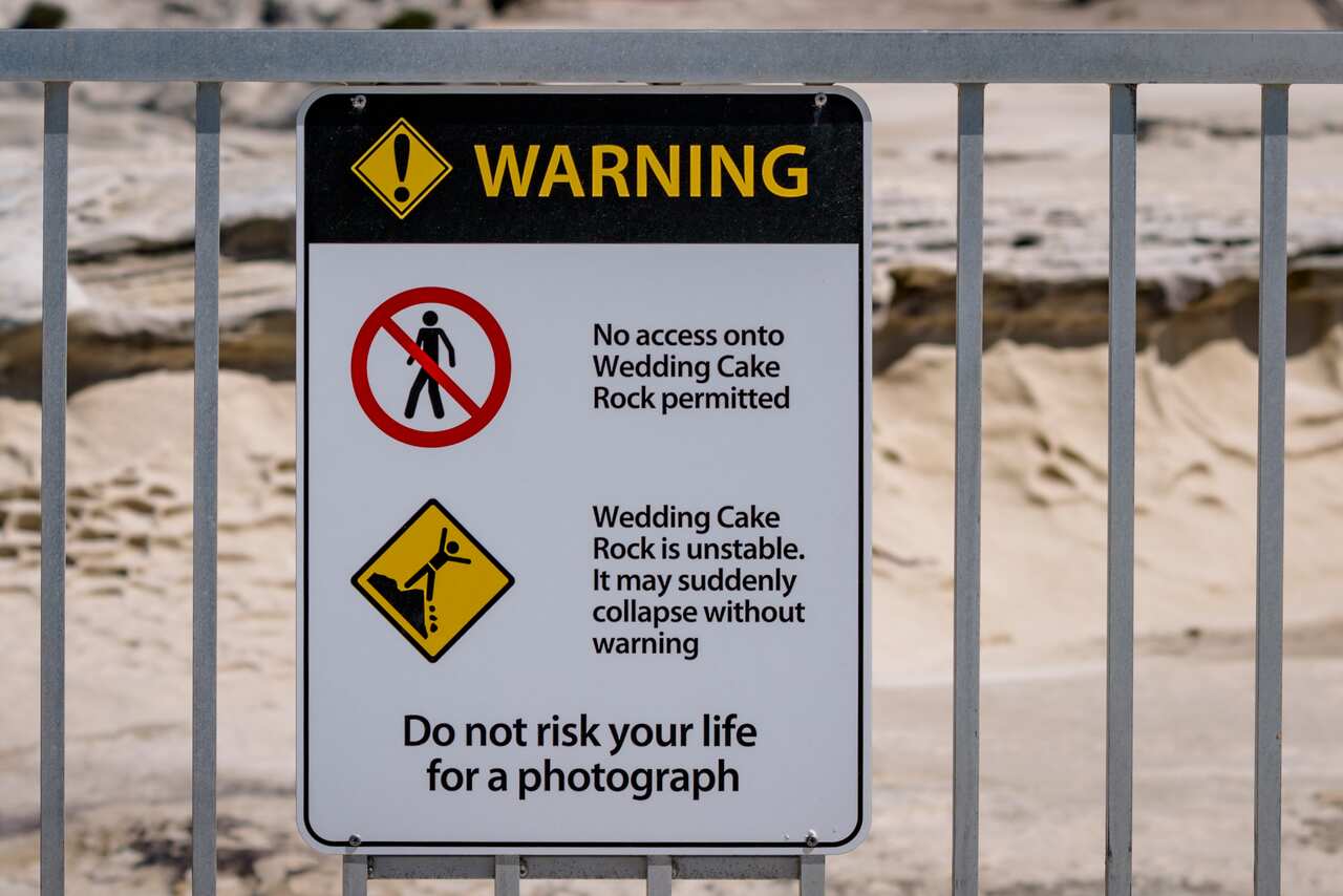 A sign on some railings that warns people to not access Wedding Cake Rock, adding "Do not risk your life for a photograph".