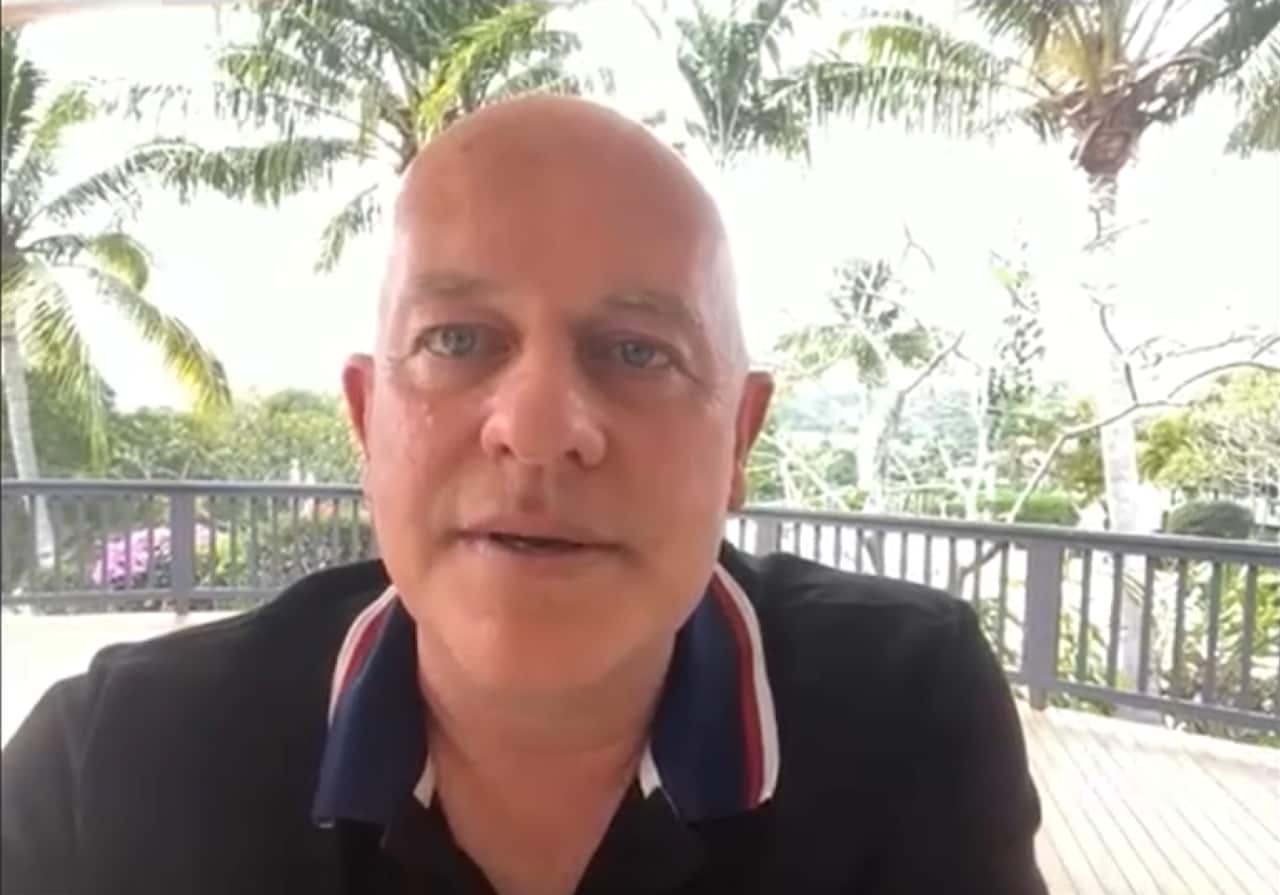 A man wearing a polo shirt speaking into a webcam