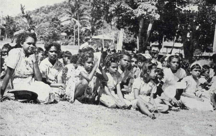 black and white photo of young aboriginal girls sitting on the ground on a reserve in the 1950s