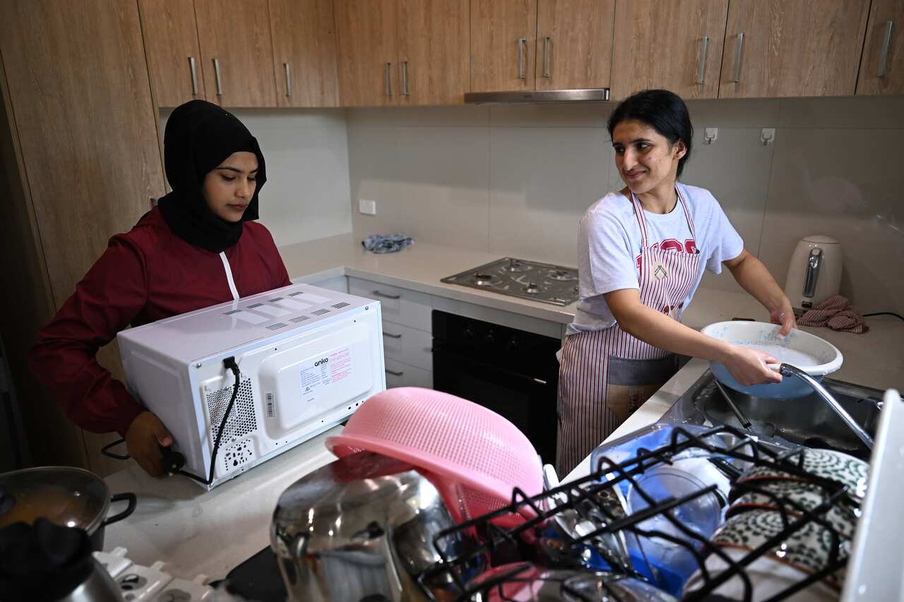 A woman puts a microwave in a kitchen while another woman washes dishes