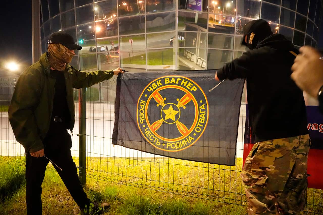 Two people hanging a flag on a fence outside a building.