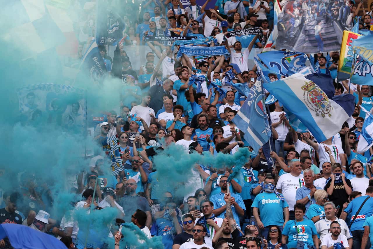 Napoli fans wearing blue and white cheer from the stands.