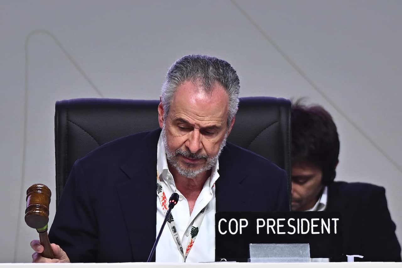A man seated at a desk, banging down a gavel. There is a sign that says "COP PRESIDENT" on the desk.