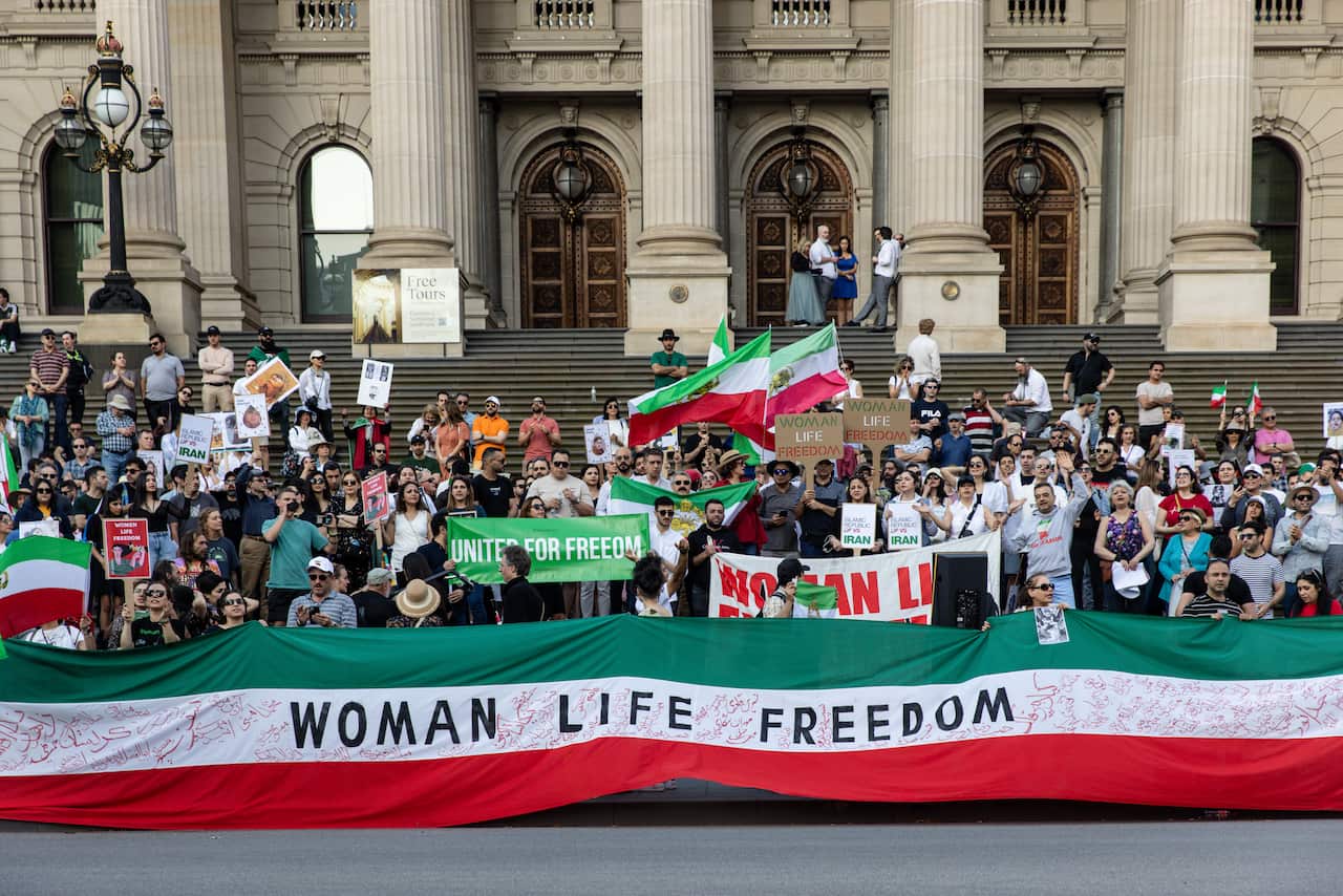 A large group of protesters holding up a sign that says Woman Life Freedom on a building's steps.