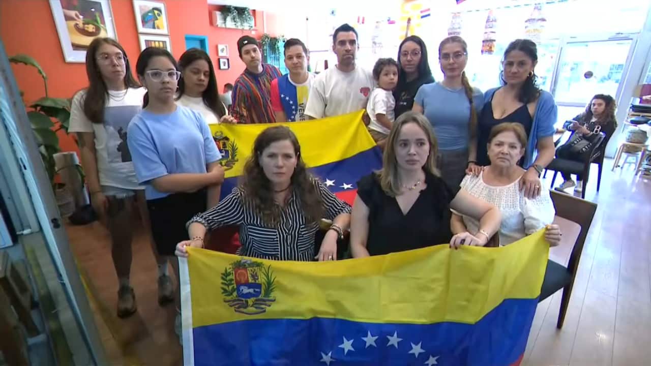 A group of people, some standing and others sitting, inside a restaurant holding Venezuelan flags. 