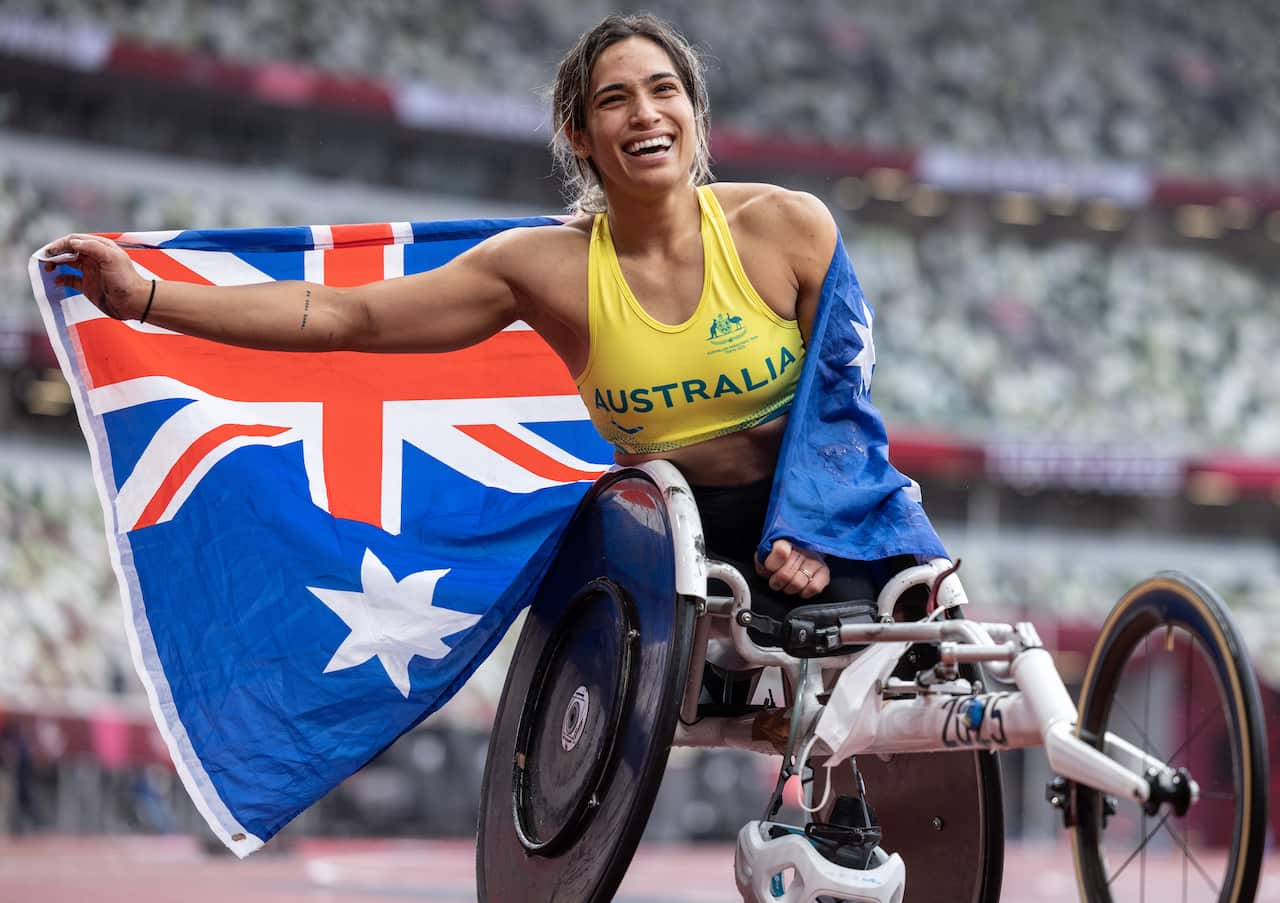 A woman in a wheelchair with the Australian flag draped over her shoulder. A massive crowd is in the background. 