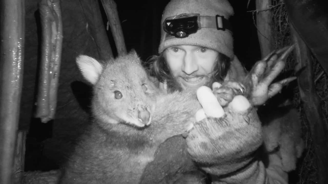 A greyscale image of a man holding a pademelon.