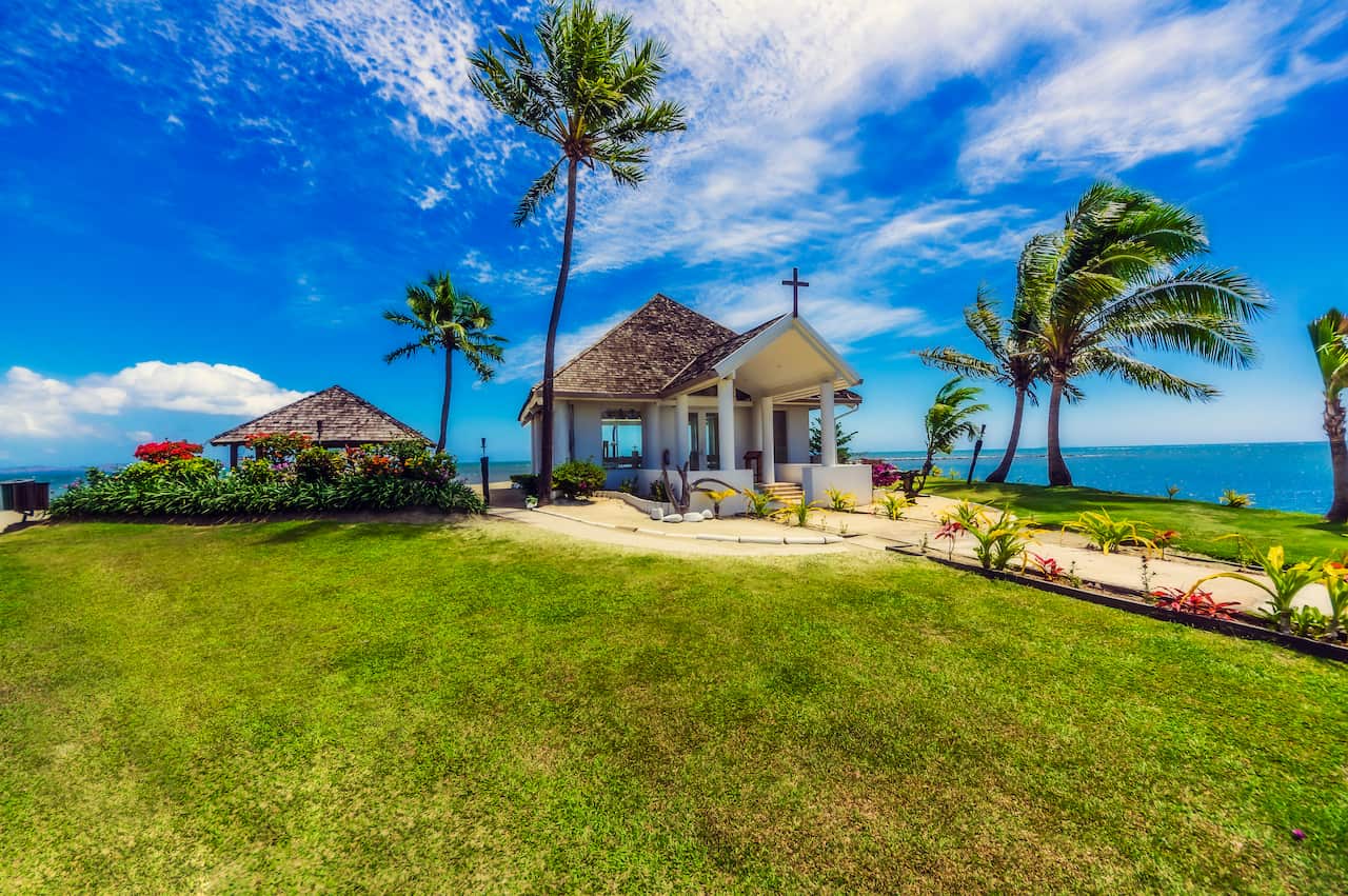 Chapel by the beach with white sand and tropical palm trees.