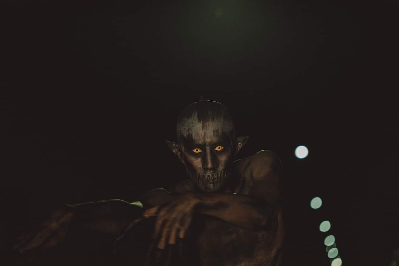 A creepy figure with yellow eyes lurks down a dark street