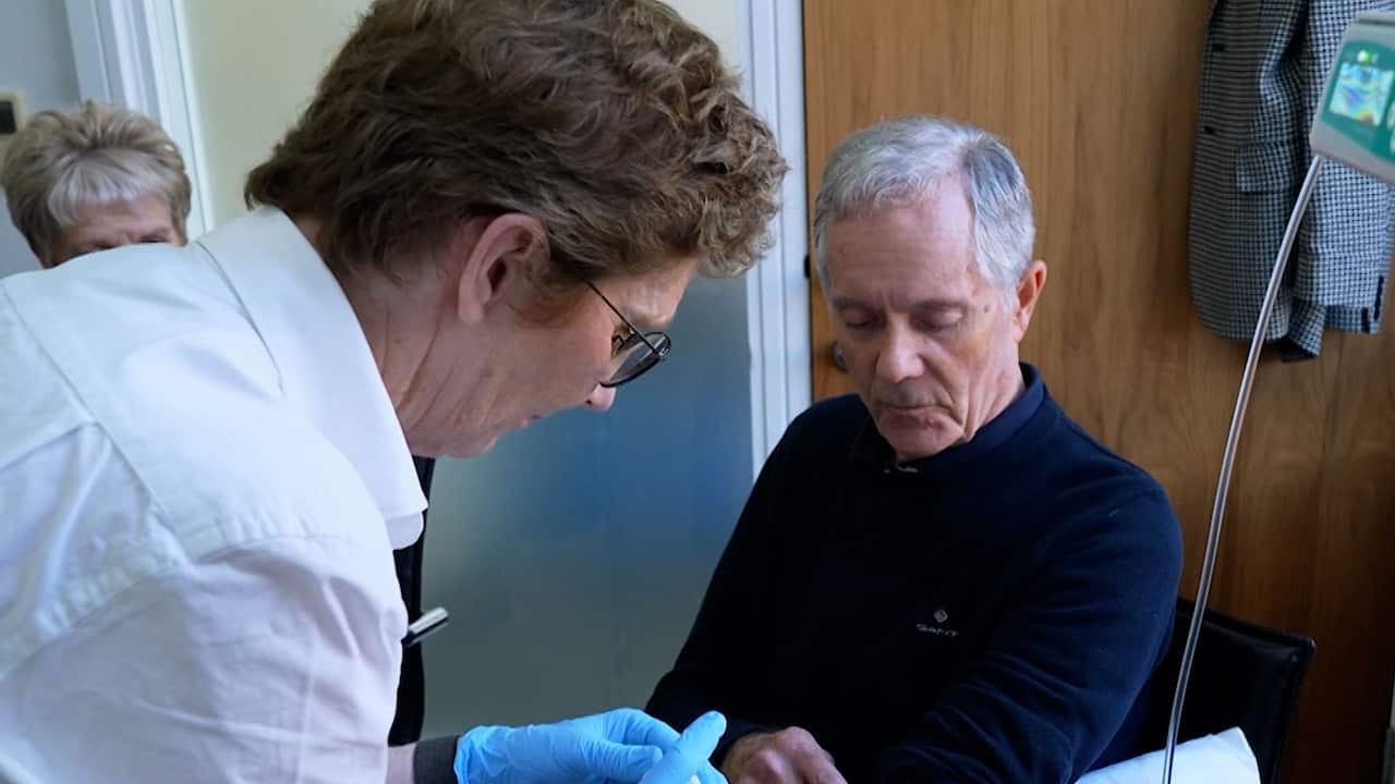 A woman in medical scrub administering an injection to a grey-haired elderly man