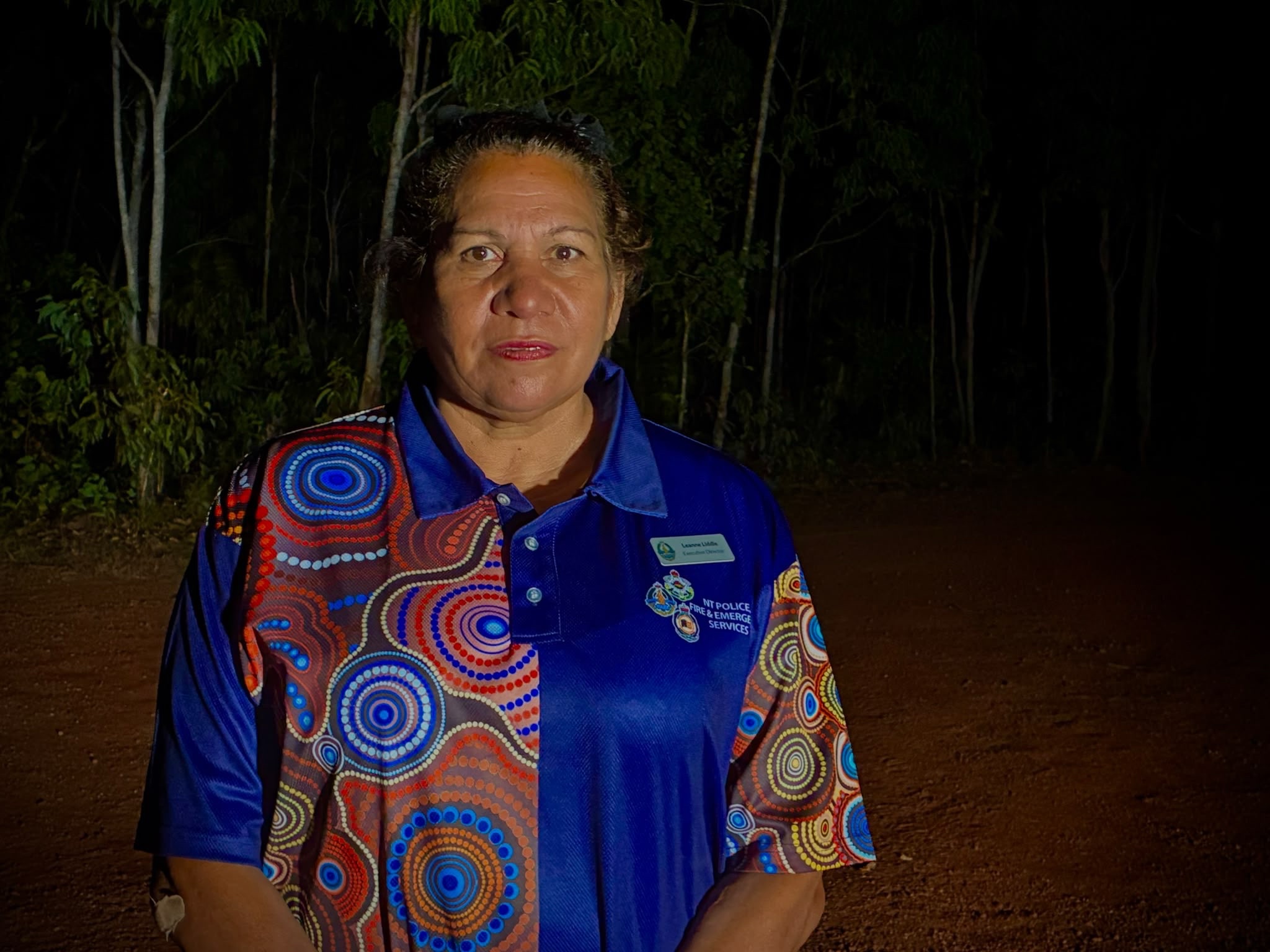 A middle-aged Indigenous woman, wearing a blue shirt with Indigenous artwork embroidered on it.