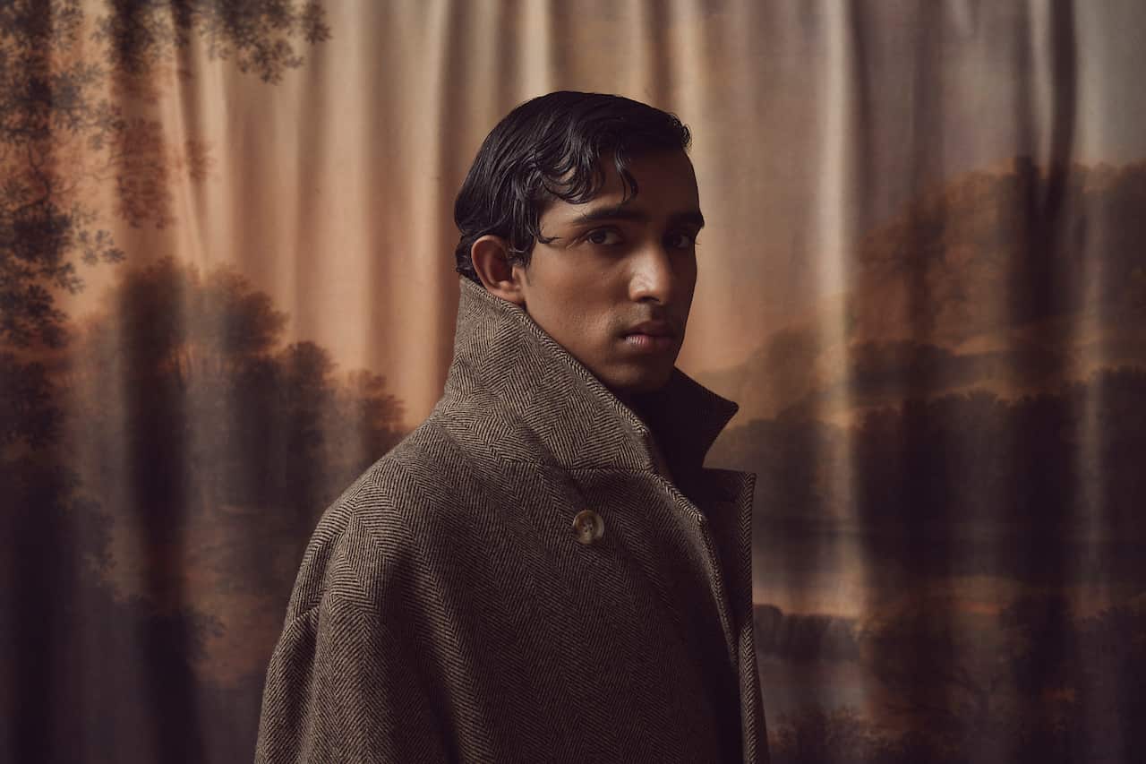 A side profile of a male model wearing a coat with the collar pulled up.