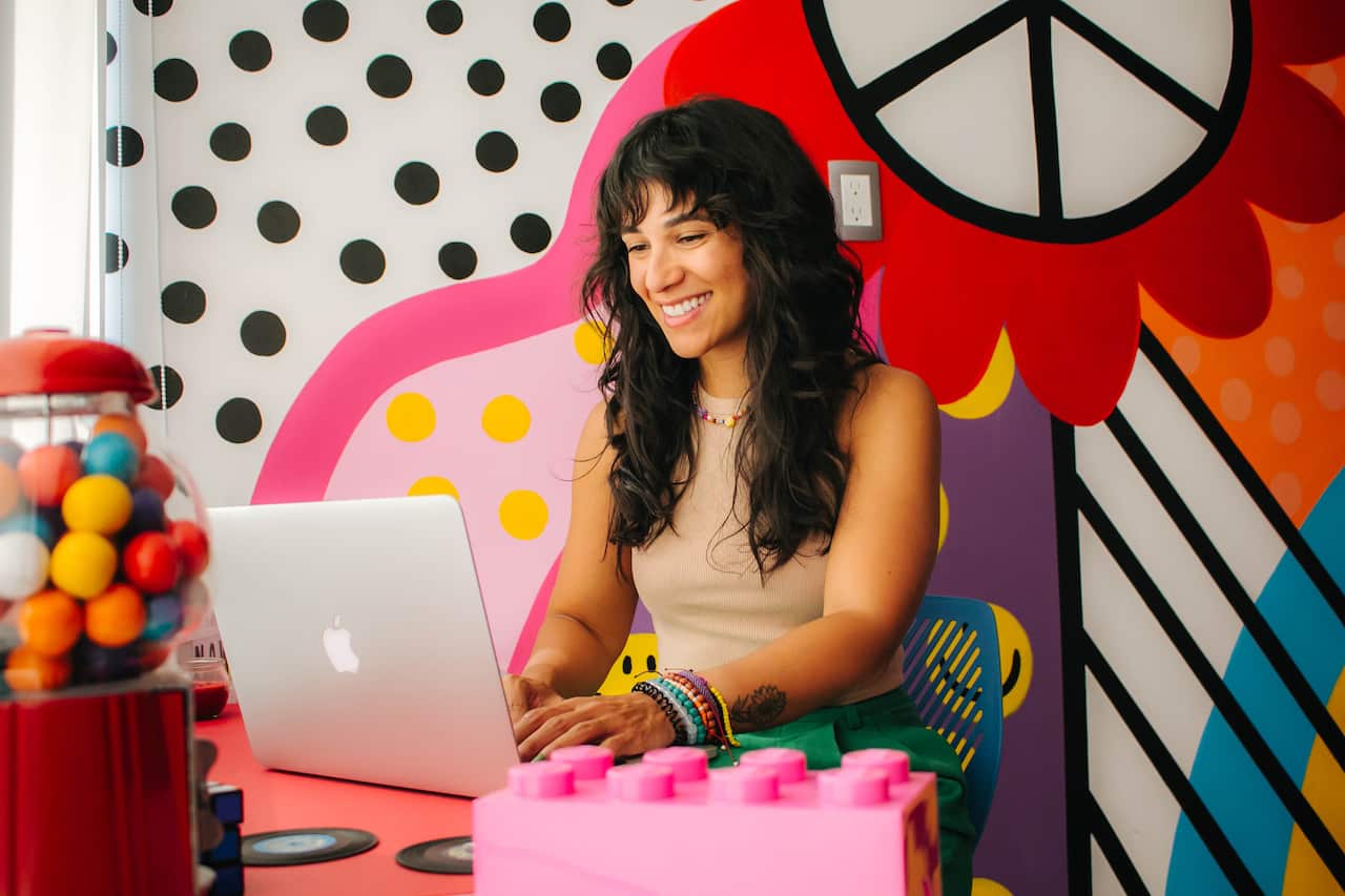 A woman working on her laptop in front of a colorful wall