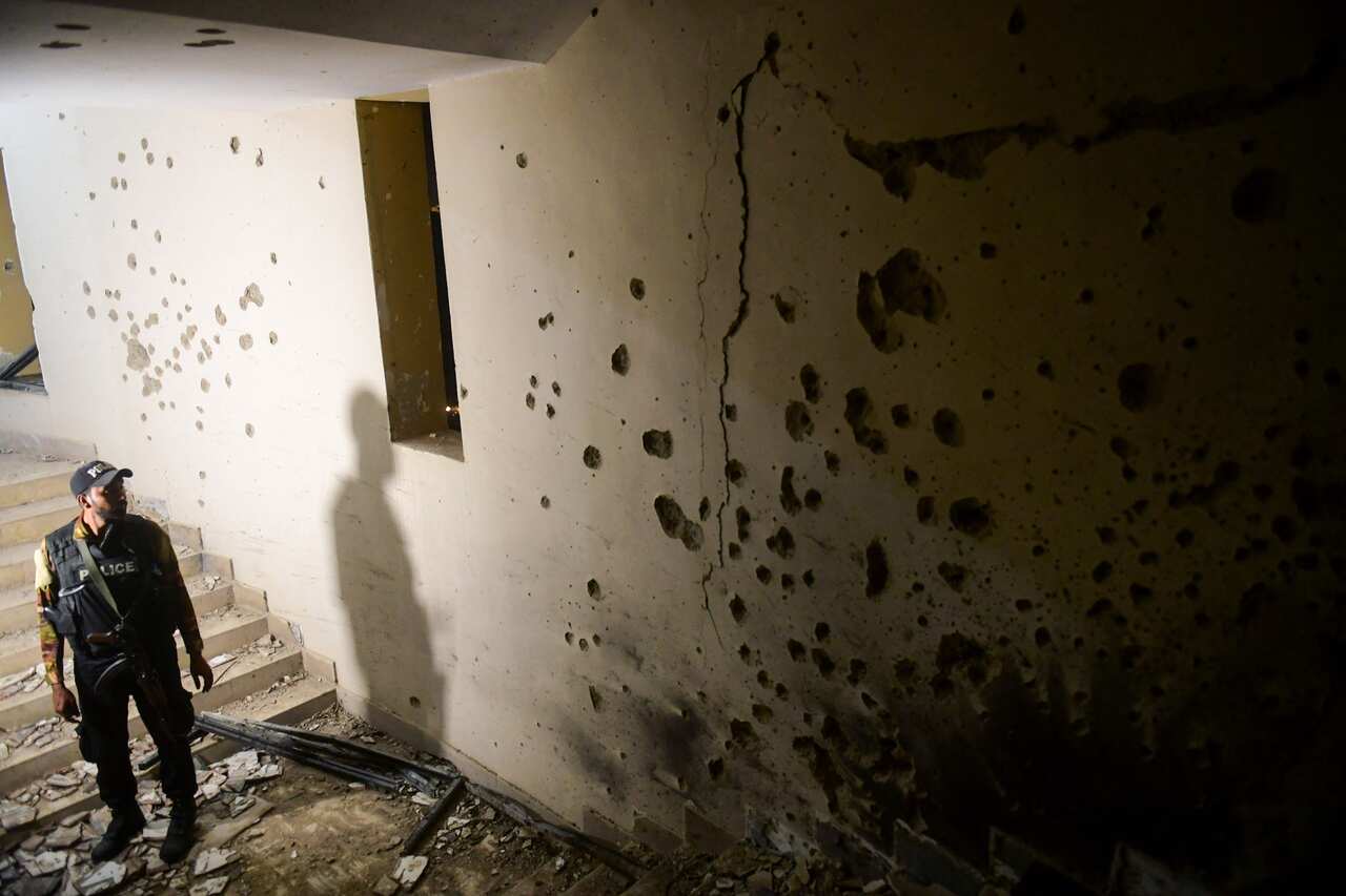 Policeman looks at a wall riddled with bullet holes.
