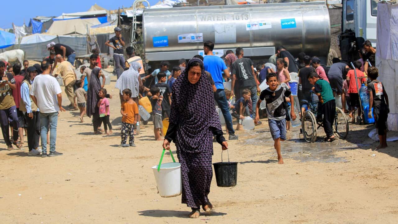A Palestinian woman collects water from an aid tanker