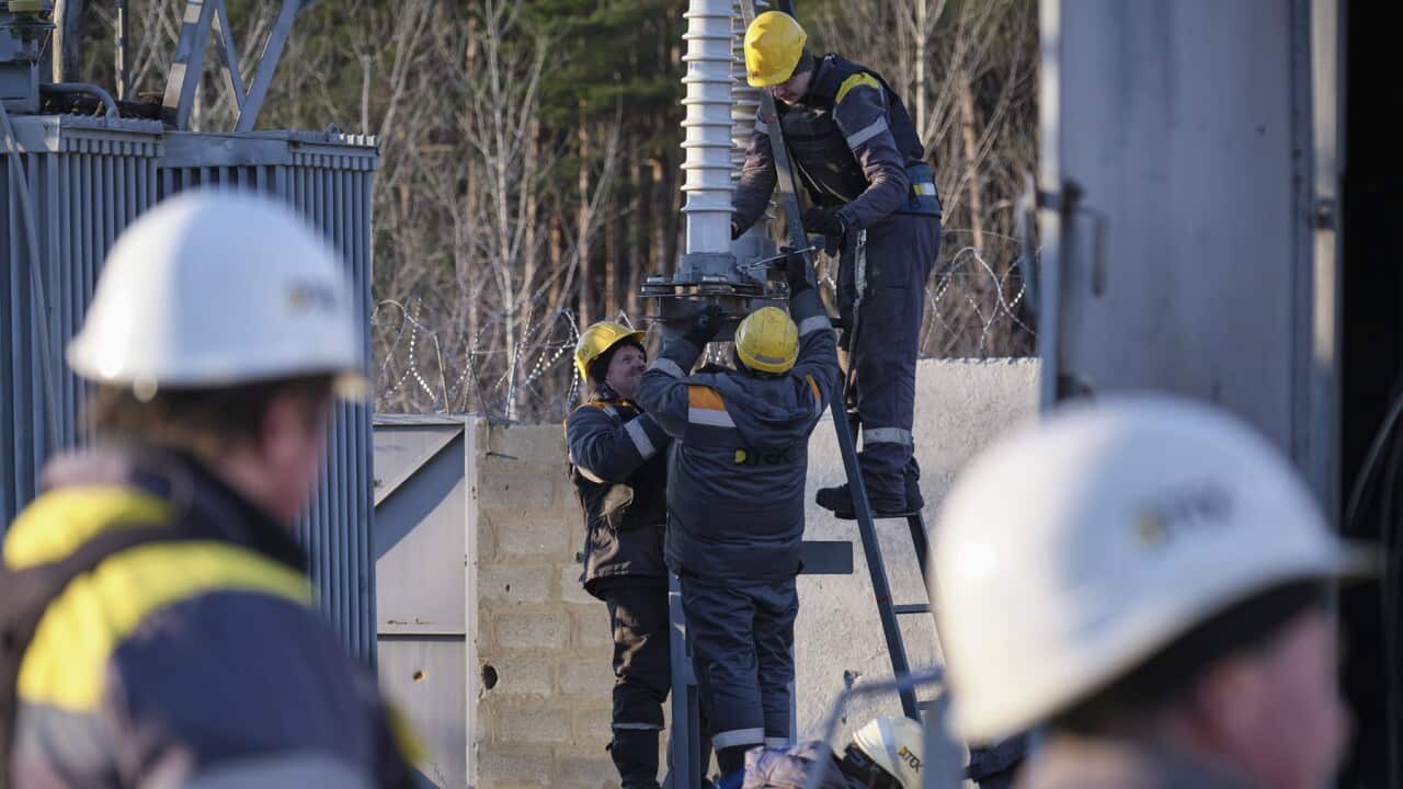 Ukrainian engineers stand on a ladder trying to repair electricity supplies (AAP).jpg