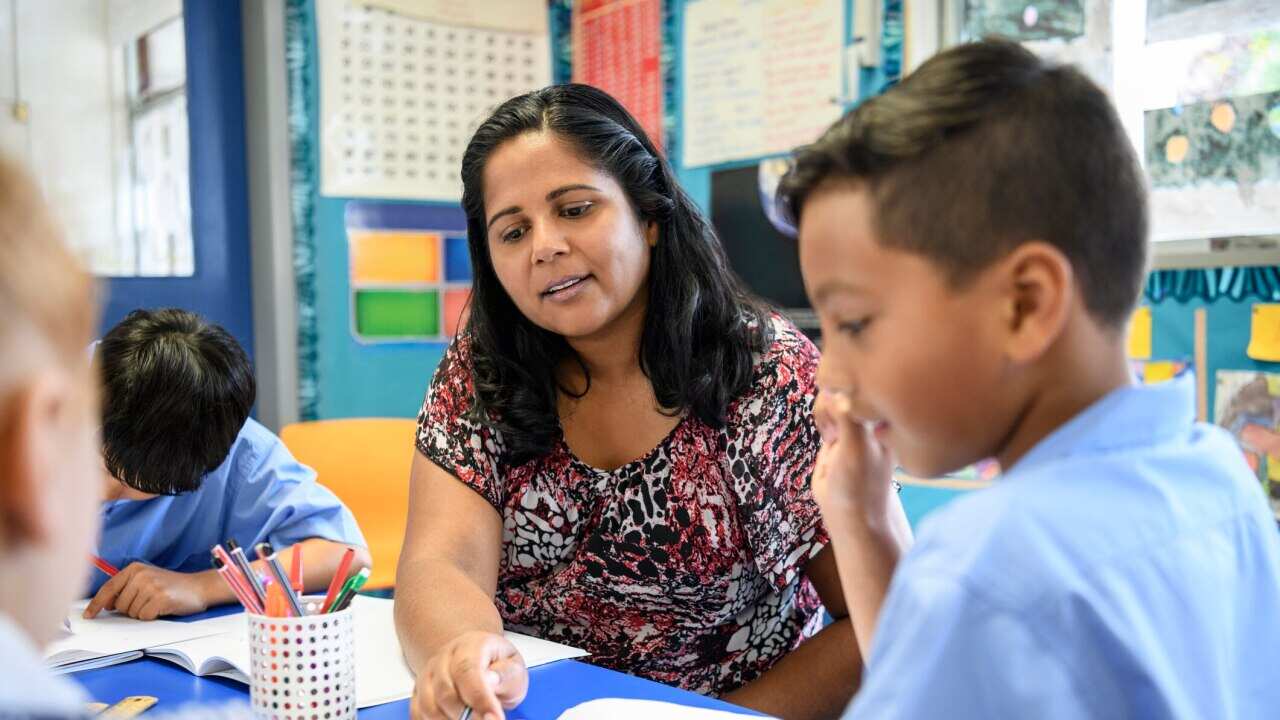 Aboriginal primary school teacher helping young boy in the classroom