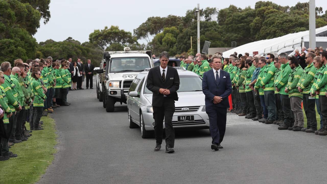 A guard of honour of Forestry and Fire Management workers lines the road as the hearse departs the funeral for veteran firefighter Bill Slade