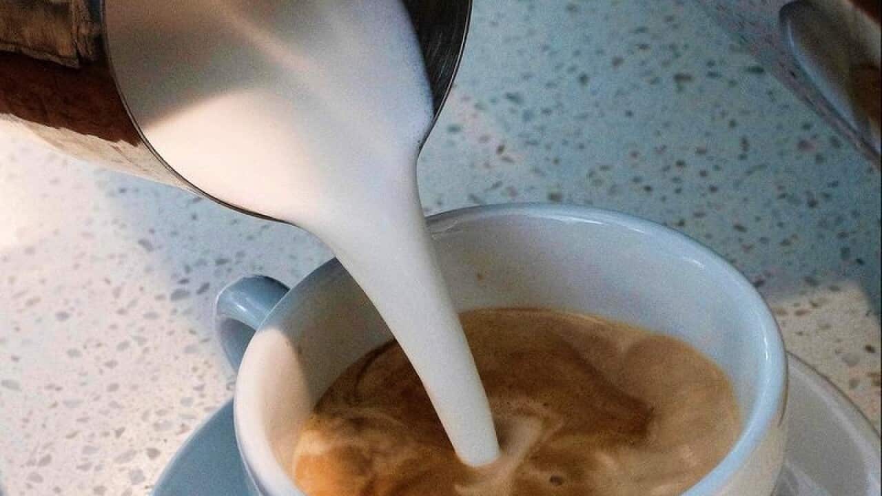 A barista pours steamed milk into a cup of coffee
