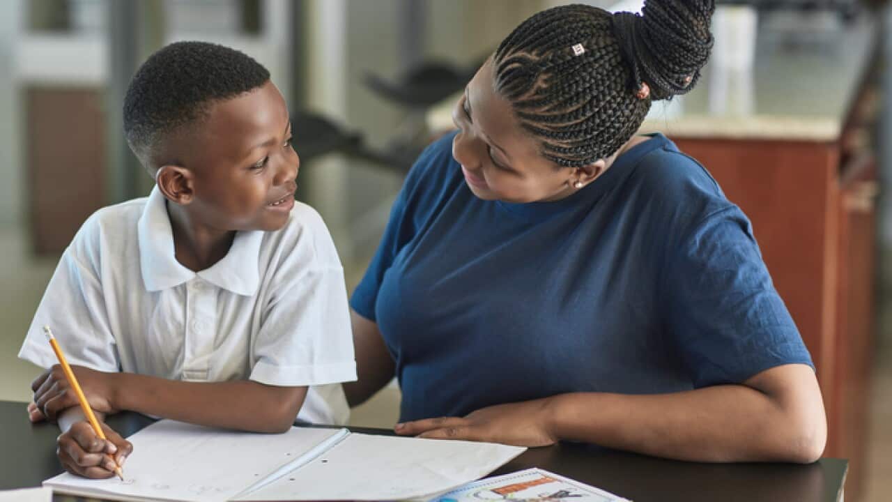 Happy woman looking at son doing homework