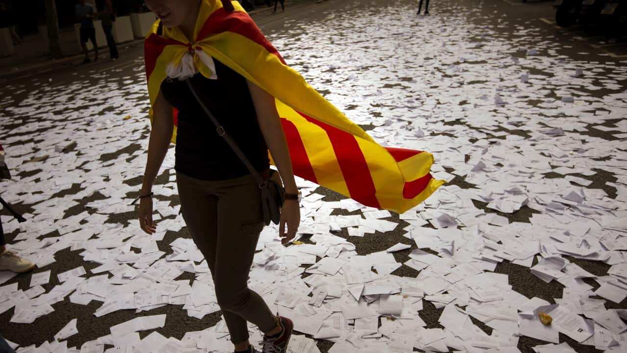 (File Image) A woman wearing an independence flag walks along a street covered with referendum ballots on October 3.