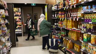A person browses products at a supermarket aisle with another person seen with a shopping basket in the background