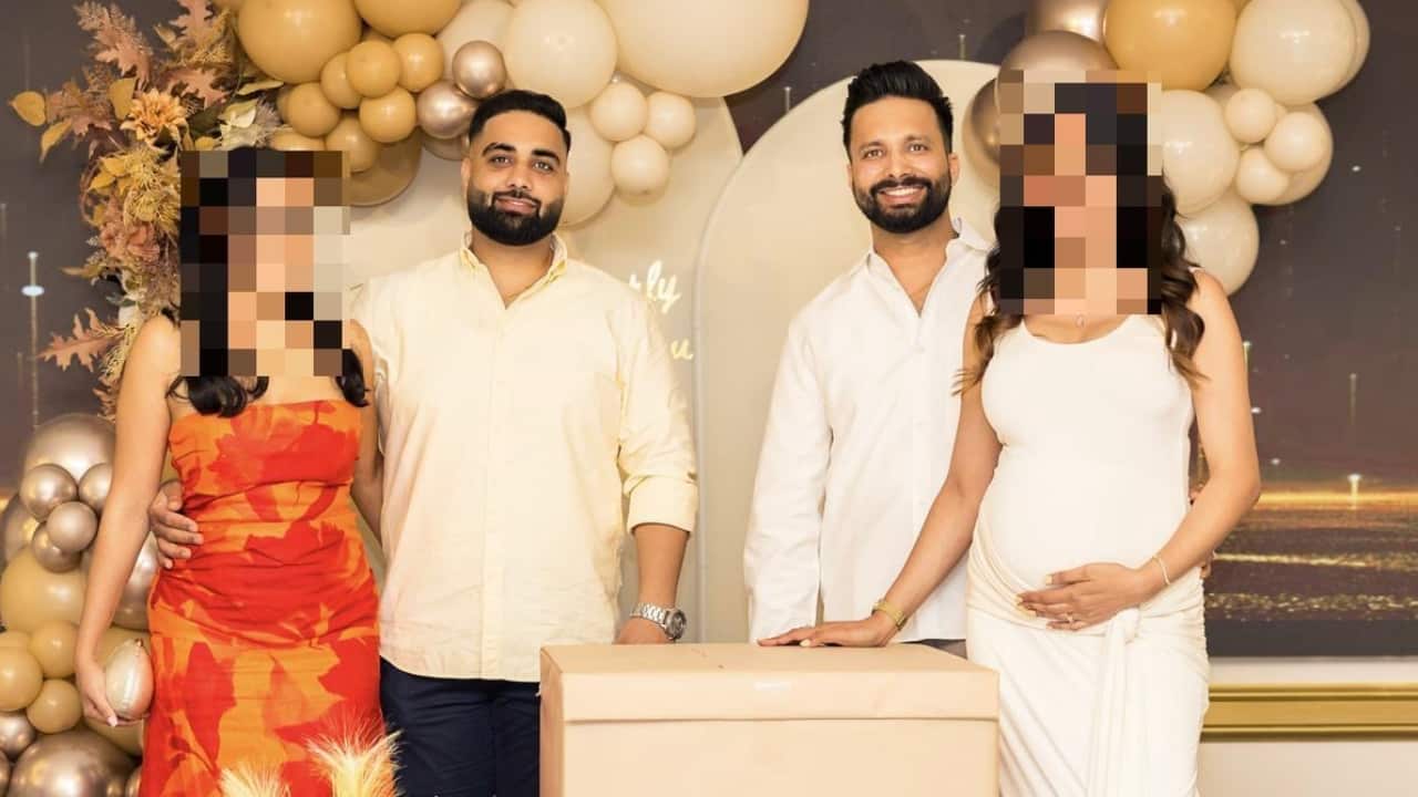 Two men standing with their partners against a backdrop of gold balloons.