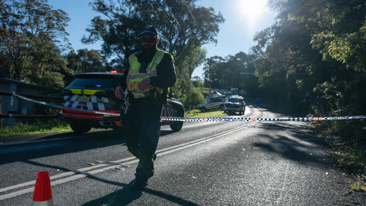 A policeman in standing in front of a cordoned-off crime scene on a road.